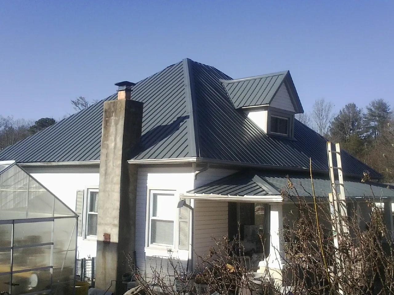 Dark blue standing seam metal roof on a white farmhouse with dormer — Slate & Tile Roof Repair by Roofing Brothers in Red Springs