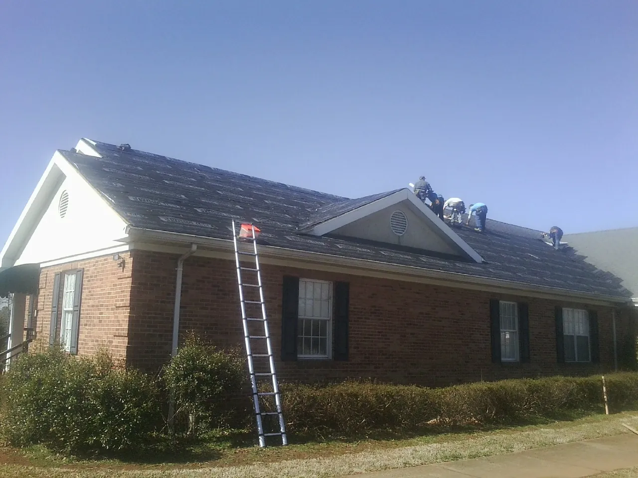 Crew tearing shingles off a brick ranch roof with a ladder set — Metal Roof Repair work by our crew in Red Springs