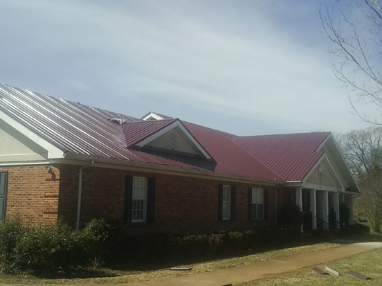 Red metal roof with gabled entries on a long brick building, from a Hail Damage Roof Repair job in Red Springs
