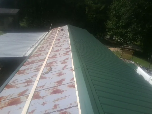 Old rusted panels beside newly installed green metal roofing — Wind Damage Roof Repair by Roofing Brothers in Red Springs