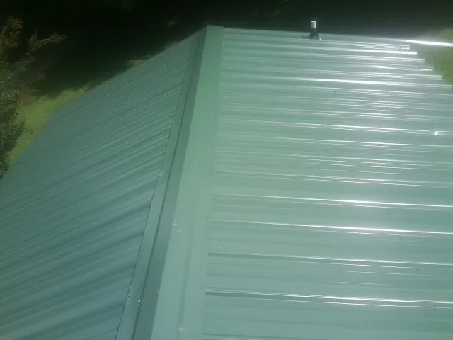 New green metal panels meeting at the ridge of a roof — Flat Roof Repair work by our crew in Red Springs