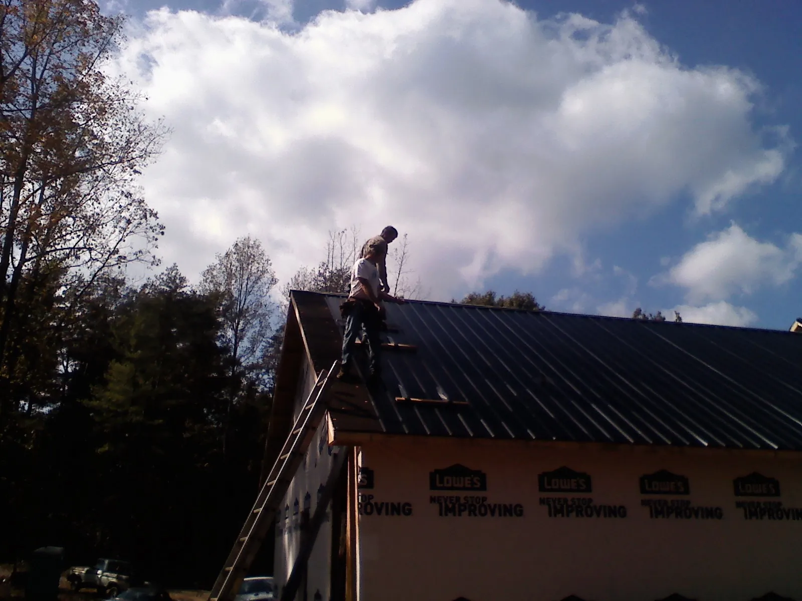 Roofer fastening dark metal panels high against a cloudy sky, from a Roof Inspection job in Red Springs