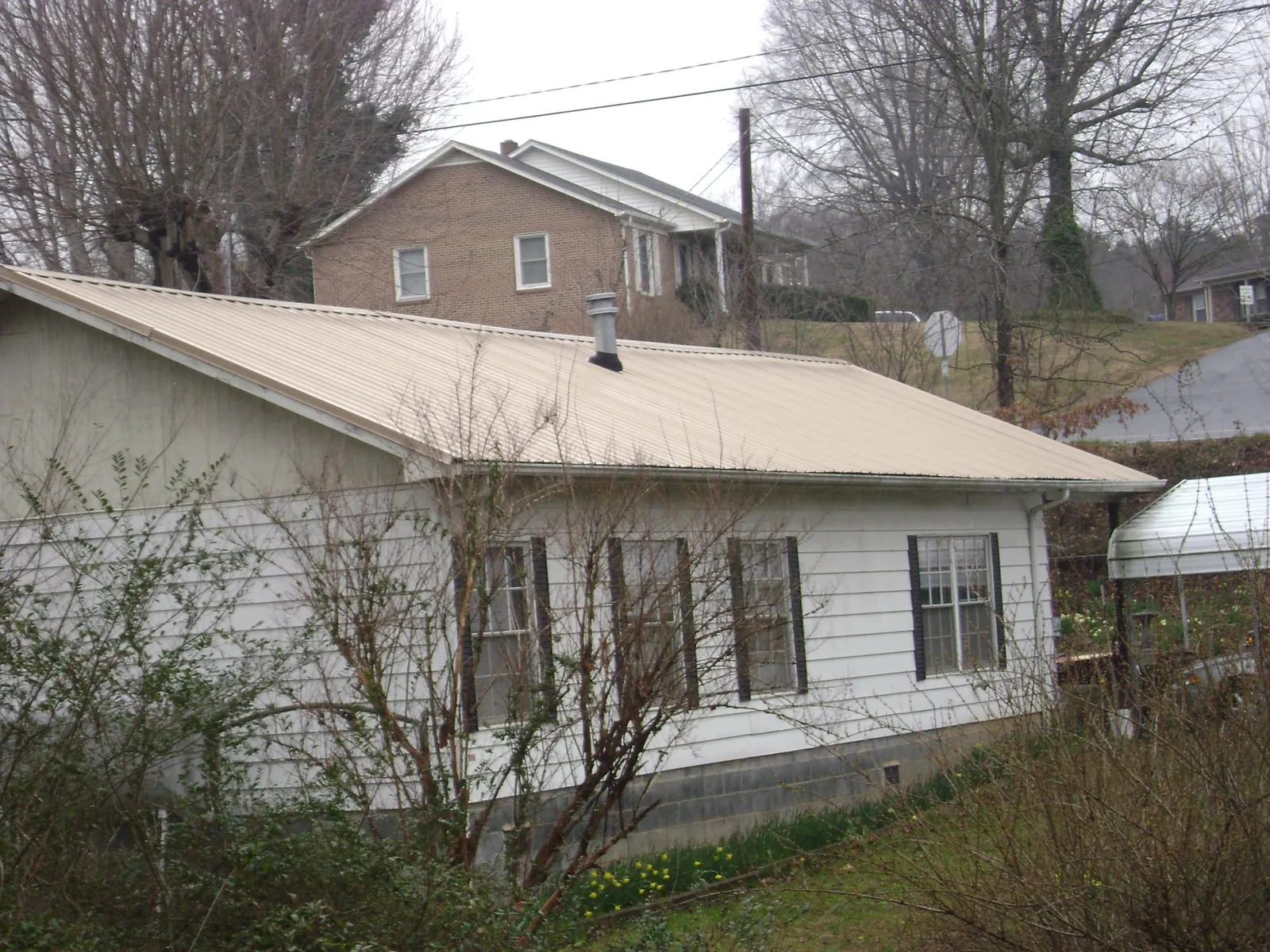 Tan metal roof on a white sided house set into a hillside — Commercial Roofing by Roofing Brothers in Red Springs