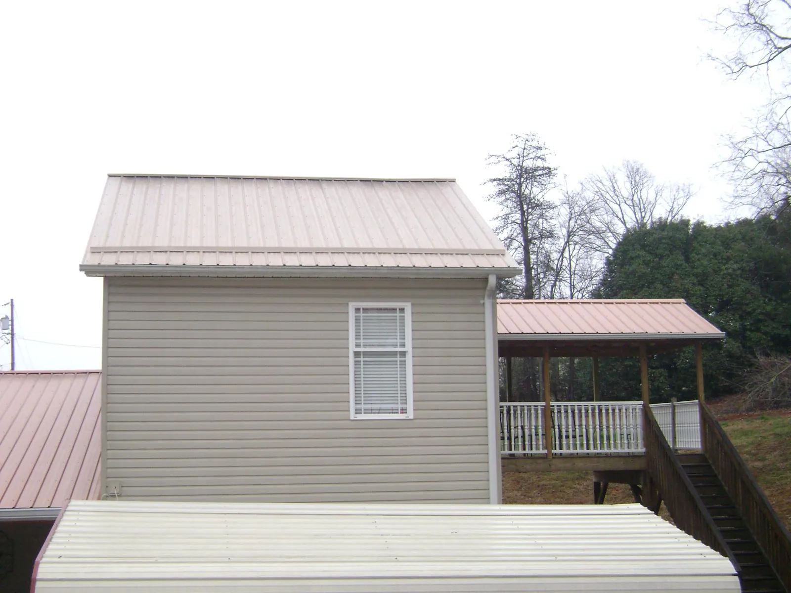 Tan metal roofs on a two story addition and attached porch, from a Roof Replacement job in Red Springs